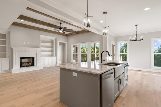 kitchen featuring appliances with stainless steel finishes, light stone counters, ceiling fan with notable chandelier, decorative light fixtures, and an island with sink