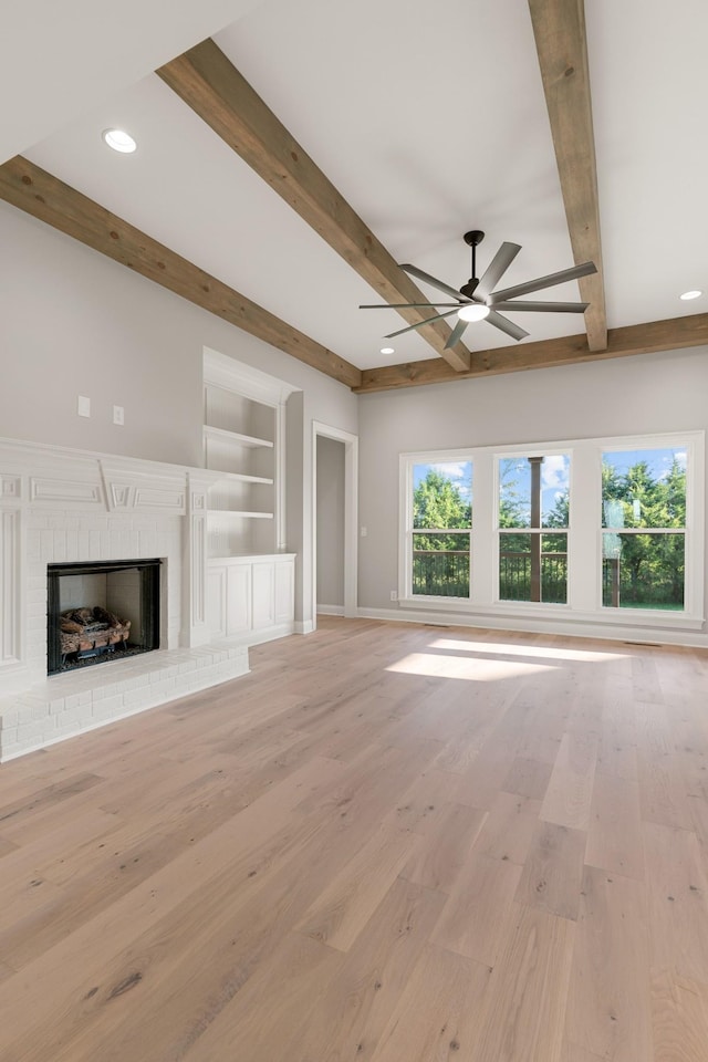 unfurnished living room featuring beam ceiling, built in shelves, a fireplace, and light wood-type flooring