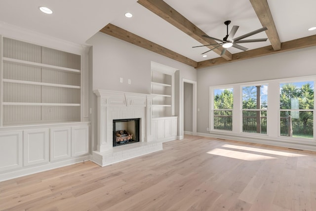 unfurnished living room with a brick fireplace, built in shelves, ceiling fan, beam ceiling, and light hardwood / wood-style floors