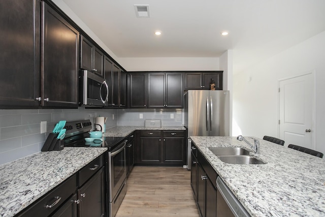 kitchen with sink, a breakfast bar area, decorative backsplash, light hardwood / wood-style floors, and stainless steel appliances