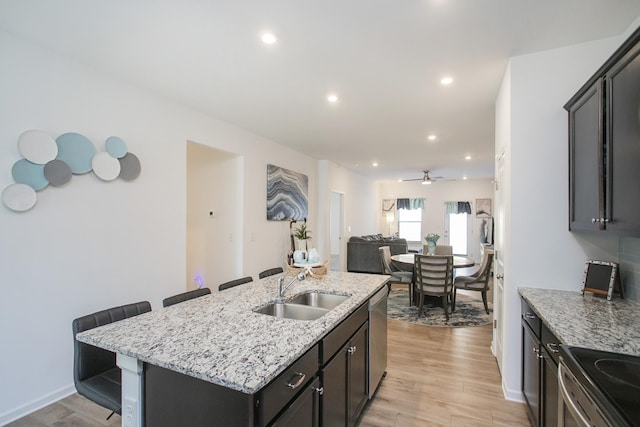 kitchen with a kitchen bar, stainless steel dishwasher, ceiling fan, sink, and an island with sink