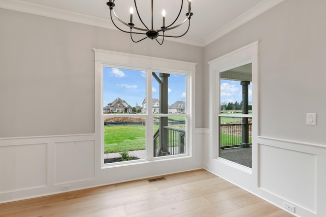 unfurnished dining area with light hardwood / wood-style flooring, ornamental molding, and an inviting chandelier