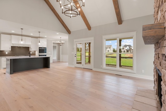 unfurnished living room featuring beam ceiling, a stone fireplace, high vaulted ceiling, and a chandelier