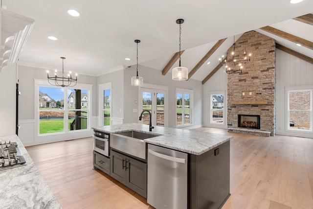 kitchen featuring stainless steel appliances, a kitchen island with sink, beam ceiling, a fireplace, and hanging light fixtures