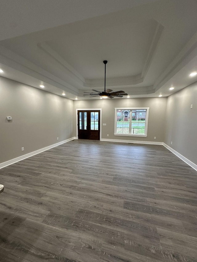 unfurnished living room featuring a raised ceiling, ceiling fan, french doors, and dark wood-type flooring