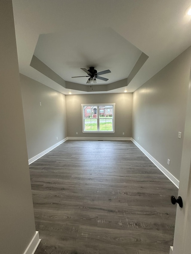 unfurnished room with a raised ceiling, ceiling fan, and dark hardwood / wood-style floors