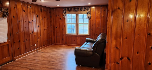 living area featuring ceiling fan, wood walls, and wood-type flooring