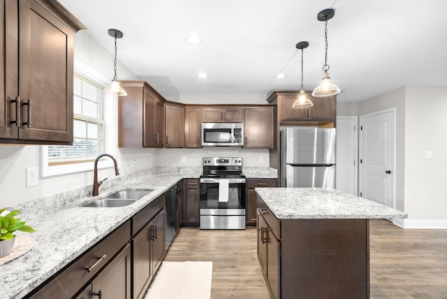 kitchen featuring sink, decorative light fixtures, light wood-type flooring, dark brown cabinets, and stainless steel appliances