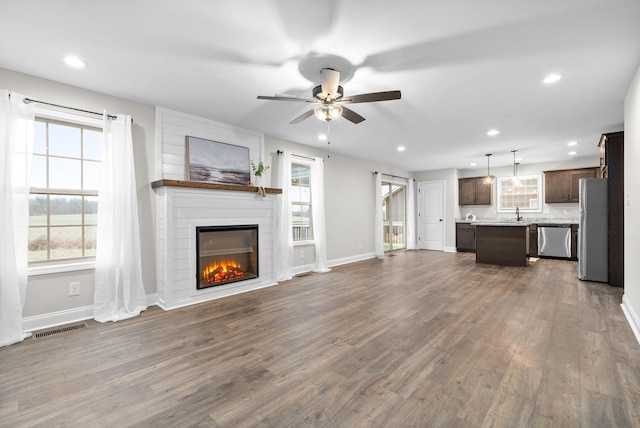 unfurnished living room featuring dark hardwood / wood-style flooring, ceiling fan, a large fireplace, and sink