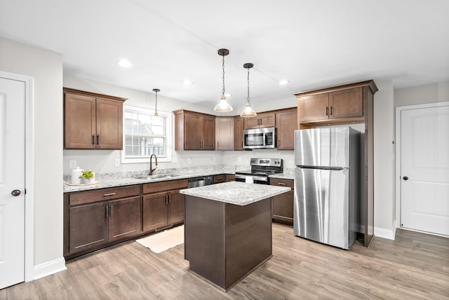 kitchen with sink, hanging light fixtures, light hardwood / wood-style flooring, a kitchen island, and appliances with stainless steel finishes