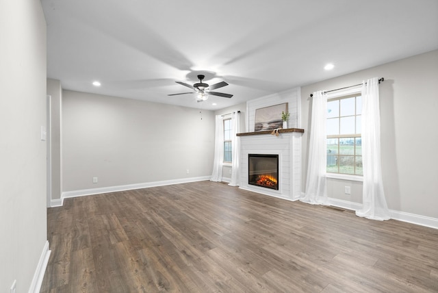 unfurnished living room featuring ceiling fan, a large fireplace, and dark hardwood / wood-style flooring