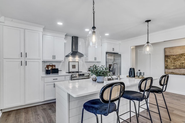 kitchen with a center island with sink, white cabinets, stainless steel appliances, and wall chimney range hood