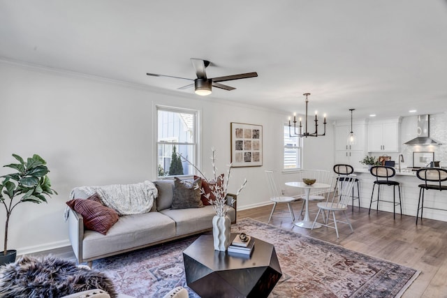 living room with hardwood / wood-style floors, ceiling fan with notable chandelier, sink, and crown molding