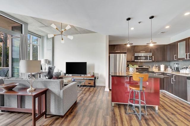 kitchen featuring dark hardwood / wood-style flooring, a kitchen bar, dark brown cabinets, a kitchen island, and appliances with stainless steel finishes