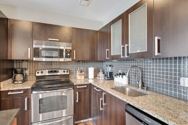 kitchen featuring sink, appliances with stainless steel finishes, tasteful backsplash, dark brown cabinets, and light stone counters