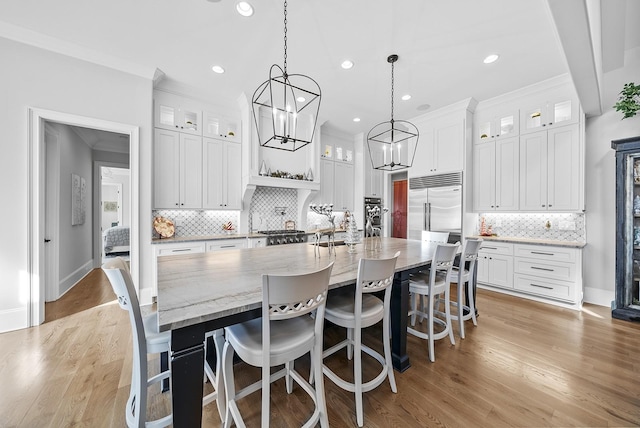 kitchen featuring a breakfast bar, a large island with sink, decorative light fixtures, white cabinets, and built in fridge