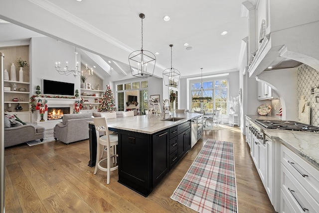 kitchen with light stone counters, stainless steel gas cooktop, sink, hanging light fixtures, and an island with sink