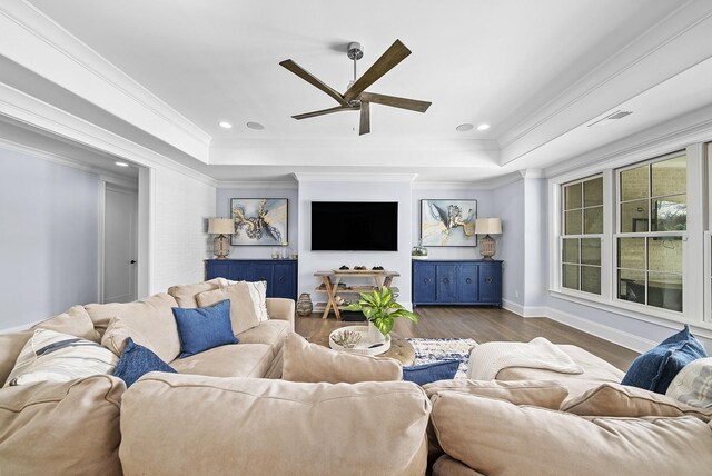 living room with a raised ceiling, crown molding, dark hardwood / wood-style flooring, and ceiling fan