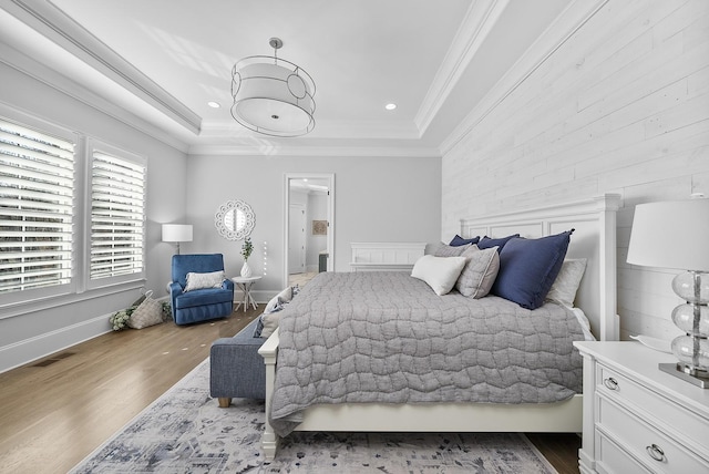 bedroom with wood-type flooring, a tray ceiling, and ornamental molding