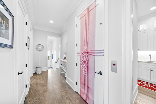 corridor with light wood-type flooring, ornamental molding, and sink