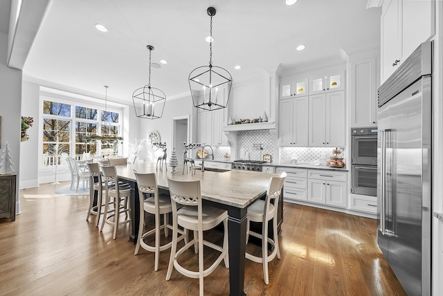 kitchen featuring white cabinets, hanging light fixtures, dark hardwood / wood-style floors, an island with sink, and stainless steel appliances