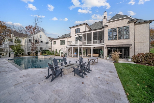 rear view of house featuring a yard, a fire pit, a patio area, and a sunroom