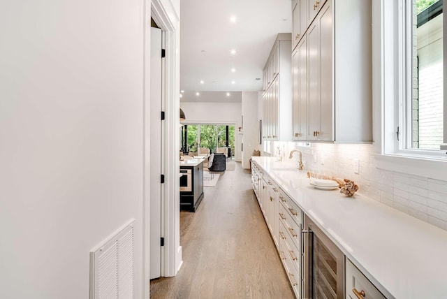 interior space with vanity, backsplash, hardwood / wood-style flooring, and wine cooler