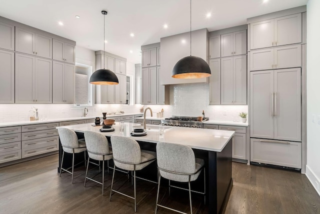 kitchen with pendant lighting, dark wood-type flooring, paneled built in fridge, and an island with sink