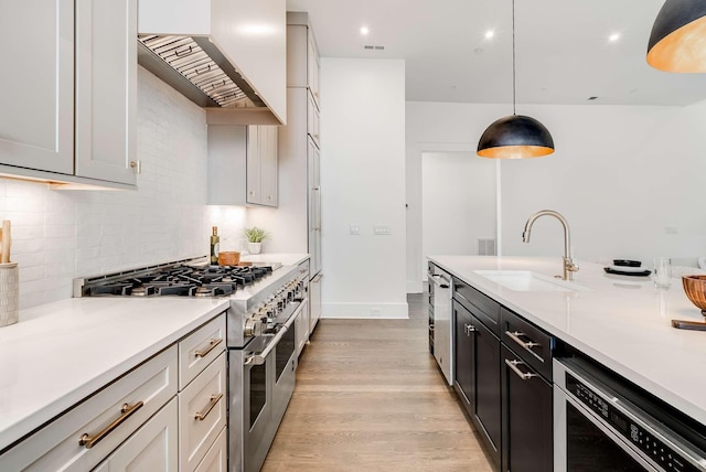 kitchen featuring sink, wall chimney exhaust hood, hanging light fixtures, range with two ovens, and dishwashing machine