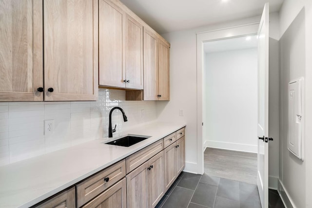 kitchen with light brown cabinetry, backsplash, dark tile patterned flooring, and sink