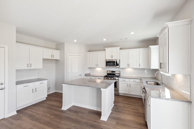 kitchen with light stone countertops, stainless steel appliances, sink, white cabinets, and a center island