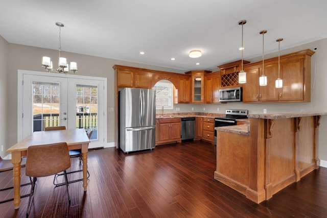 kitchen with kitchen peninsula, appliances with stainless steel finishes, french doors, a kitchen breakfast bar, and hanging light fixtures