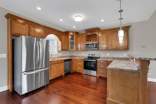 kitchen featuring kitchen peninsula, appliances with stainless steel finishes, dark wood-type flooring, sink, and decorative light fixtures