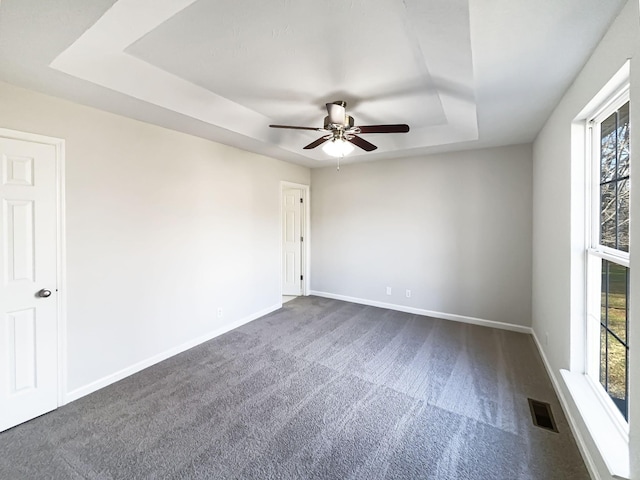 carpeted empty room with ceiling fan and a tray ceiling