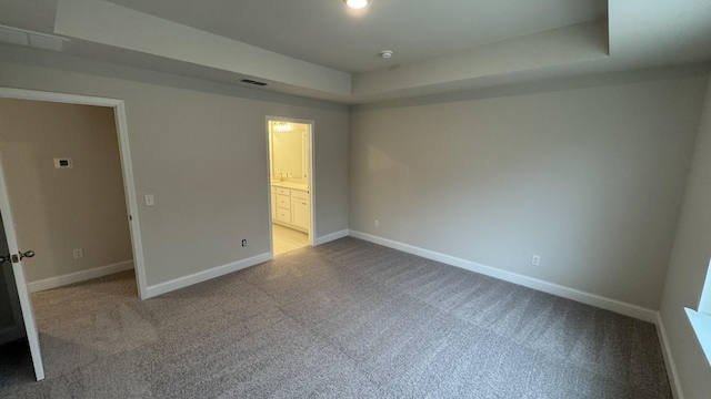 unfurnished bedroom featuring a raised ceiling, ensuite bathroom, and carpet