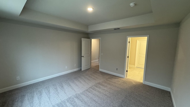 unfurnished bedroom featuring a raised ceiling and light carpet