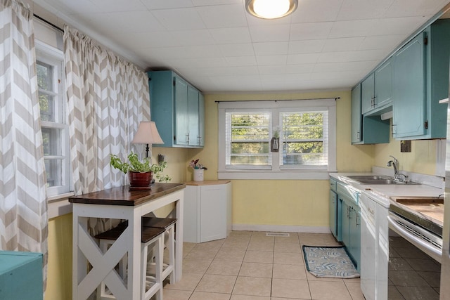 kitchen with stove, light tile patterned flooring, white dishwasher, and sink