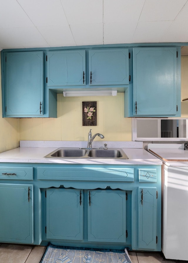 kitchen featuring stove, blue cabinets, sink, and light tile patterned floors