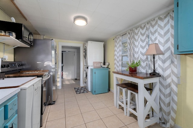 kitchen with stainless steel range with electric stovetop, light tile patterned flooring, blue cabinetry, and stacked washer and dryer