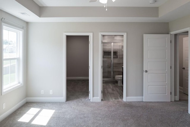 unfurnished bedroom with ensuite bath, a spacious closet, ceiling fan, a raised ceiling, and carpet floors