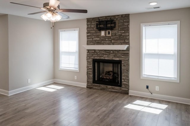 unfurnished living room with wood-type flooring, a stone fireplace, and ceiling fan