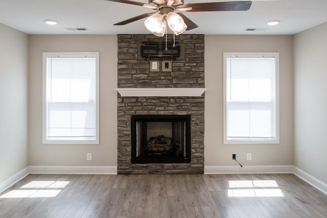 unfurnished living room with ceiling fan, light hardwood / wood-style floors, and a stone fireplace