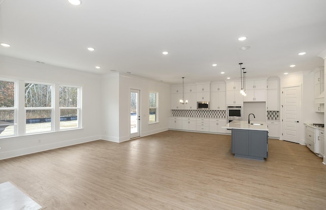 kitchen with sink, hanging light fixtures, a center island with sink, and a healthy amount of sunlight