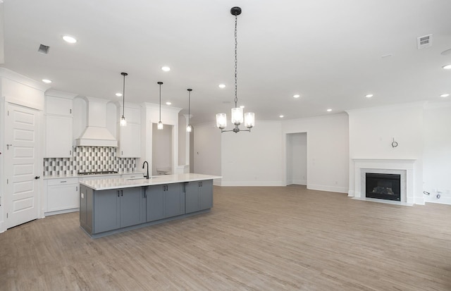 kitchen with custom exhaust hood, tasteful backsplash, hanging light fixtures, a large island with sink, and white cabinets