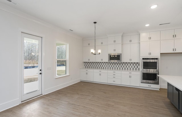 kitchen featuring tasteful backsplash, appliances with stainless steel finishes, white cabinetry, and hanging light fixtures