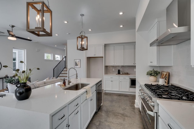 kitchen with pendant lighting, white cabinetry, sink, stainless steel appliances, and wall chimney exhaust hood