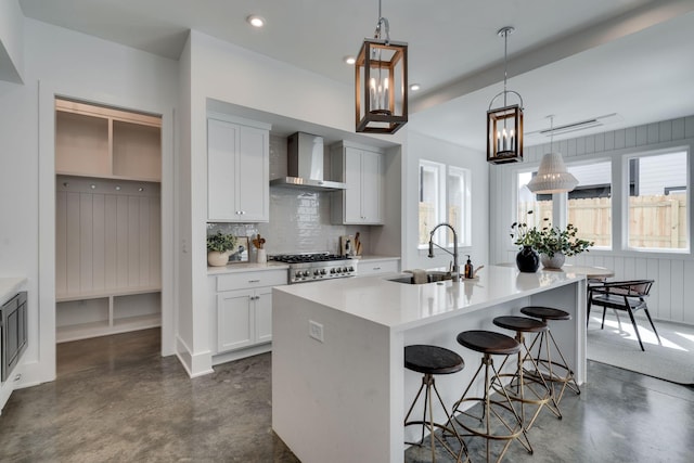 kitchen with pendant lighting, white cabinetry, sink, and wall chimney range hood