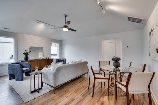 living room with ceiling fan, rail lighting, vaulted ceiling, and light wood-type flooring