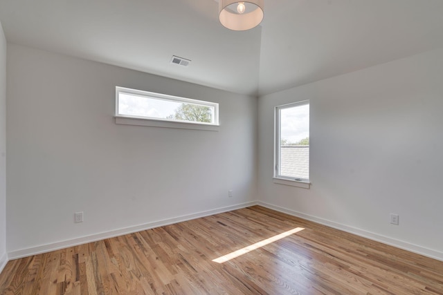 unfurnished room featuring lofted ceiling, a wealth of natural light, and light hardwood / wood-style floors