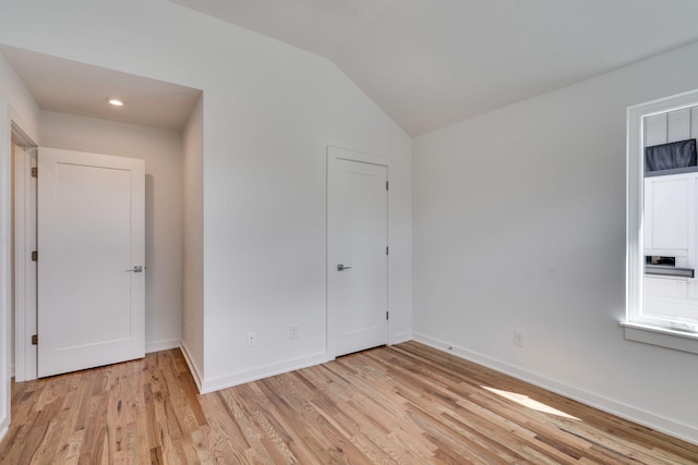 unfurnished bedroom with vaulted ceiling and light wood-type flooring